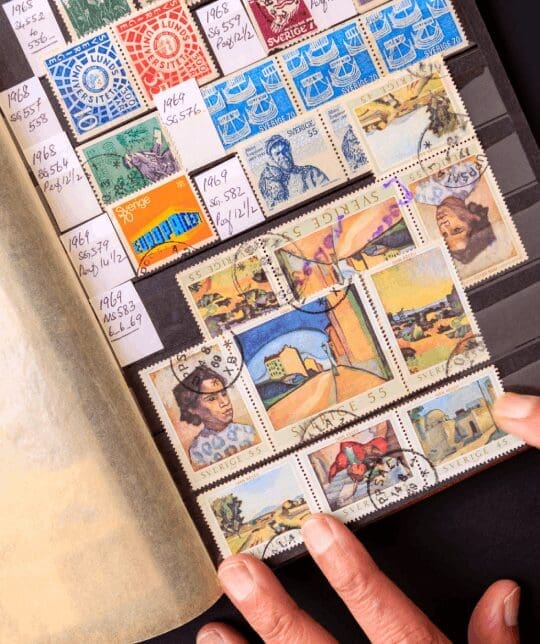 Hands flipping through a colorful stamp collection.